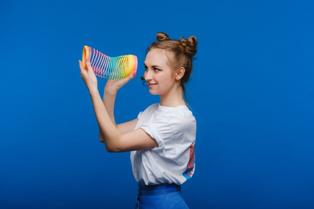 Hermosa joven jugando con un arco iris furtivo, un juguete de su infancia en un azul