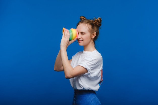 Hermosa joven jugando con un arco iris furtivo en una pared azul