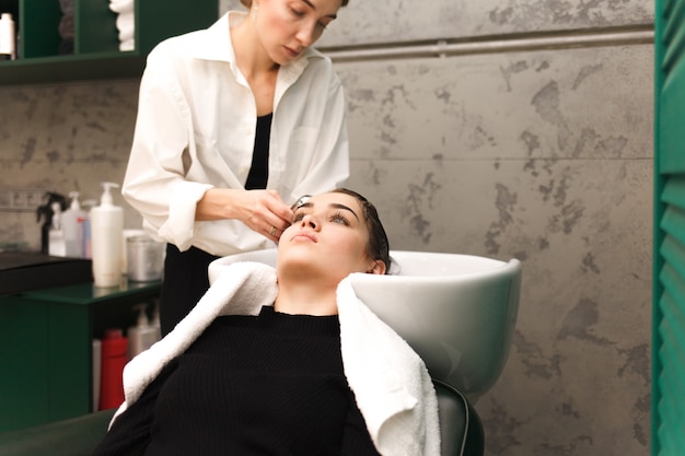 Hermosa joven se lava la cabeza con una belleza. El peluquero está lavando el cabello para el cliente