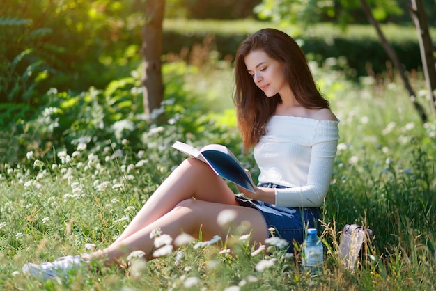 Hermosa joven lee un libro en un parque de verano al aire libre.