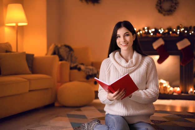 Hermosa joven leyendo el libro en casa en la víspera de navidad