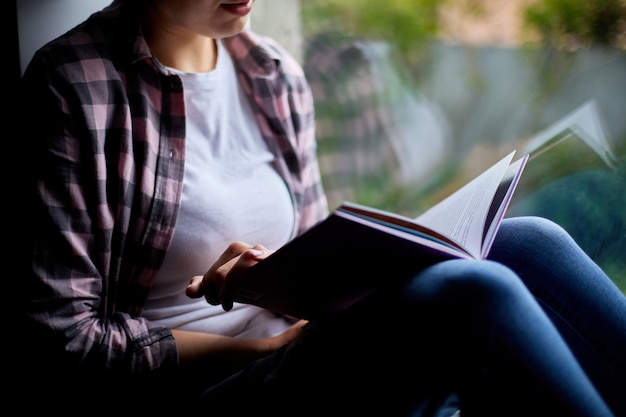 Hermosa joven leyendo libro junto a la ventana en casa