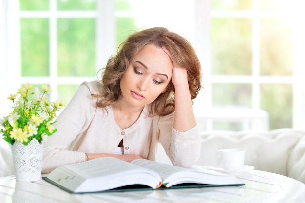 Hermosa joven leyendo un libro sobre una cocina ligera y acogedora