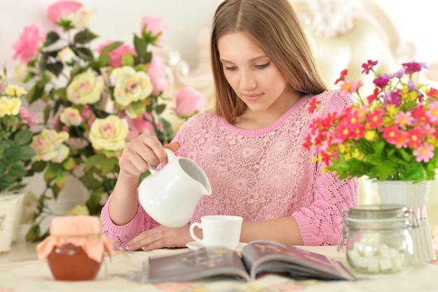 Hermosa joven leyendo una revista y bebiendo té