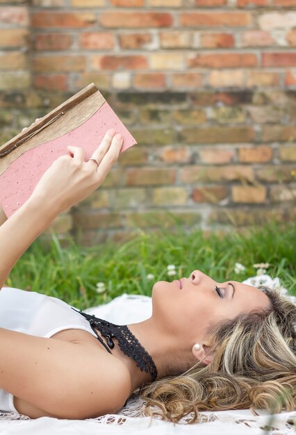 Hermosa joven con libro tirado en el césped