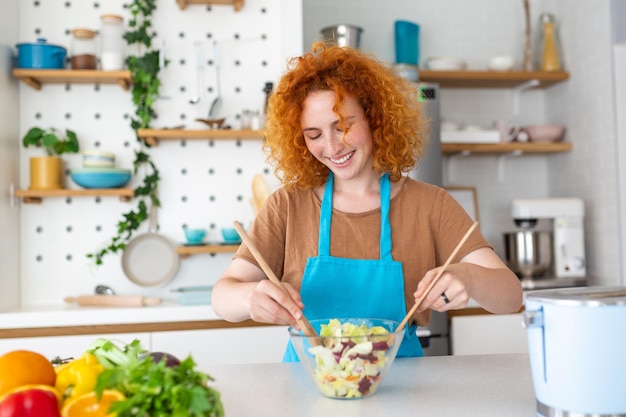 Una hermosa joven y linda mujer sonriente en la cocina está preparando una ensalada vegana con ropa casual