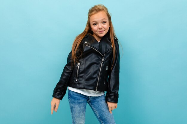 Hermosa joven en un look casual con una chaqueta de cuero y jeans posando en azul claro