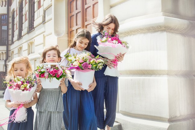 Hermosa joven madre adulta y sus pequeñas hijas alegres y felices con ramos de flores