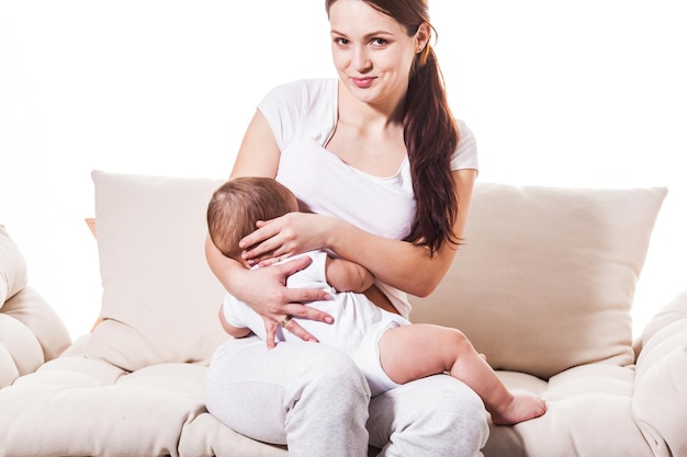 La hermosa joven madre amamanta el pecho de su bebé mientras está sentada en un sofá