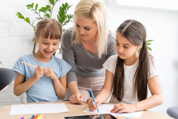 Hermosa joven madre ayudando a sus hijas con la tarea.