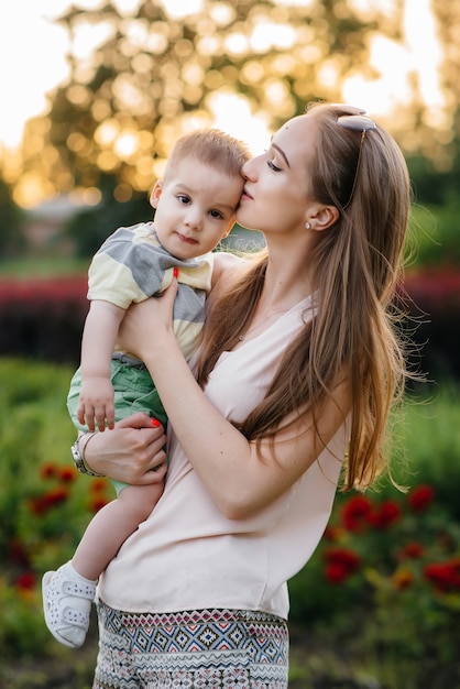 Una hermosa joven madre besa y abraza a su pequeño hijo durante la puesta de sol en el parque. Paseo familiar feliz en el parque.