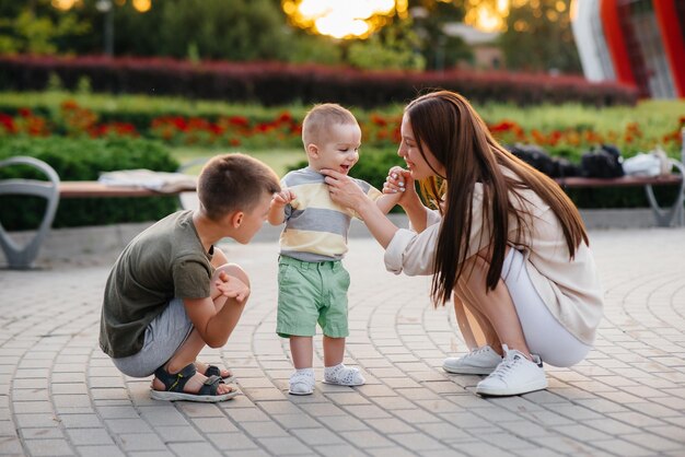 Una hermosa joven madre con dos niños pequeños está jugando en el parque durante la puesta de sol. Caminata familiar feliz con niños en el parque.