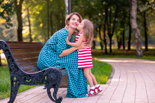 Hermosa joven madre e hija en un cálido día soleado de verano. Familia feliz madre e hija pequeña hija jugando y caminando en el parque y disfrutando de la hermosa naturaleza.