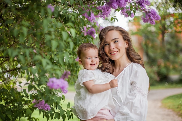 Hermosa joven madre e hija cerca de la lila floreciente. Primavera.