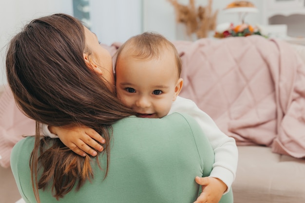 Una hermosa joven madre está sentada en el piso de la sala y abraza a su pequeño bebé. Una familia feliz.