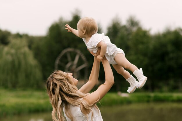 Una hermosa joven madre con una hija de un año en la naturaleza, mamá sonríe y arroja a su hija