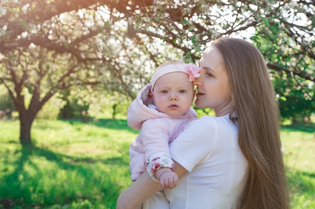 Hermosa joven madre huggs pequeña hija. Caminando con bebé en el parque. Ternura y cuidado