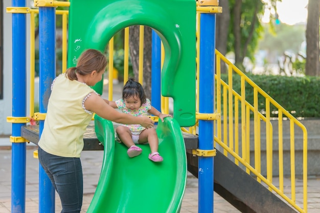 Hermosa joven madre juega con su hija con diversión en el patio de recreoFeliz día de la madreGente de Tailandia