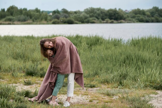 Hermosa joven madre jugando con su pequeña hija junto al río en la naturaleza