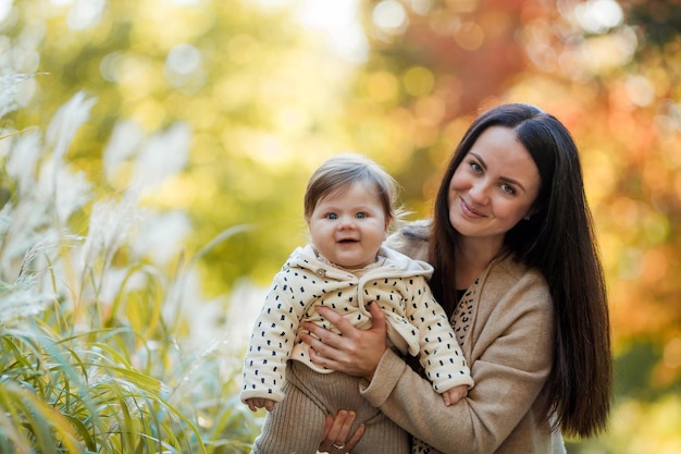 Hermosa joven madre con una linda niña de 7 meses camina en el parque de otoño Retrato de una familia feliz Caída