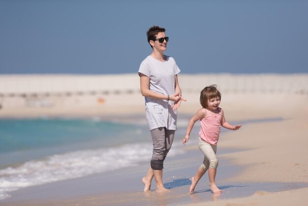 hermosa joven madre y linda niña disfrutan mientras corren en una playa exótica a lo largo del océano Viajes y vacaciones.