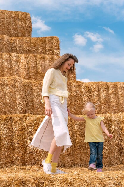 Hermosa joven madre con una niña pequeña en los enormes montones de heno en la granja Vacaciones de verano en el campo