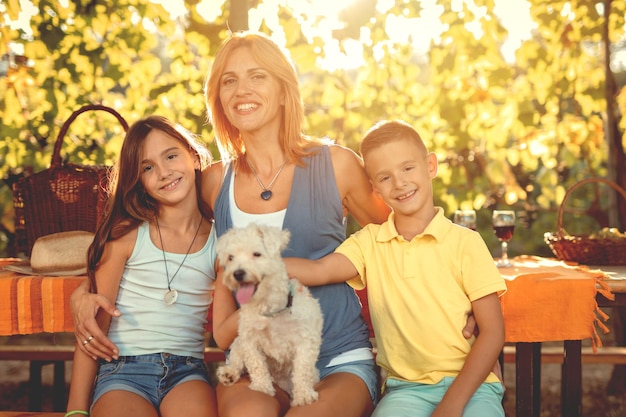 Foto hermosa joven madre sonriente con sus hijos y su perro haciendo un picnic en un viñedo.