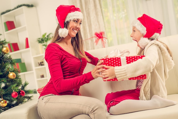 Hermosa joven madre sorprende a su linda niñita con Presente para Navidad o Año Nuevo.