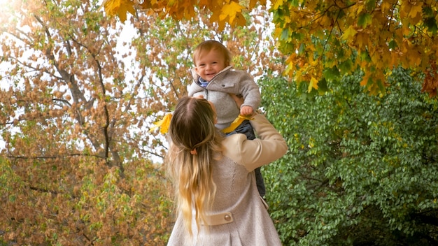 Hermosa joven madre sosteniendo y vomitando a su pequeño hijo en el parque de otoño.