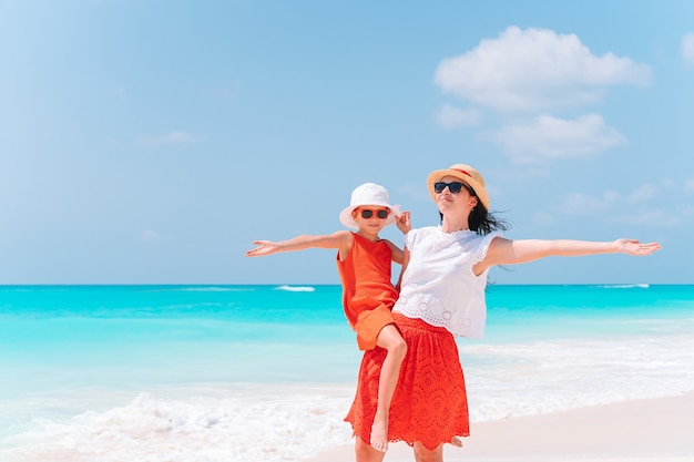 Hermosa joven madre y su adorable hijita se divierten en la playa tropical