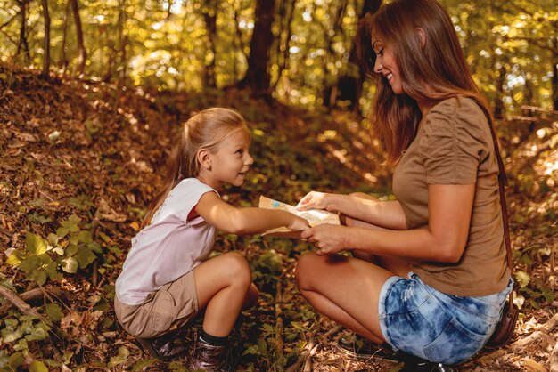 Hermosa joven madre y su hija en el bosque mirando el mapa para encontrar la dirección.