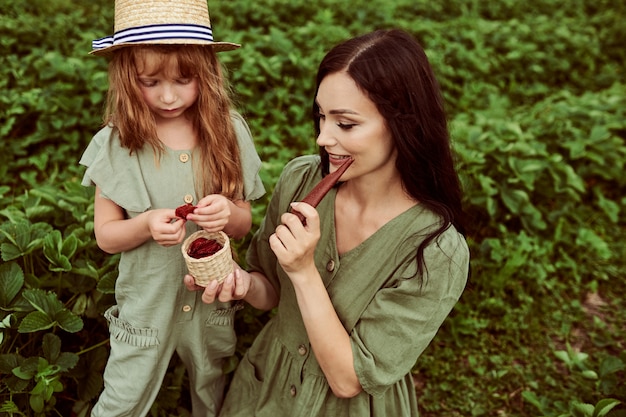 Hermosa joven madre con su hija divirtiéndose en un campo verde con fresas