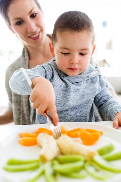 Foto hermosa joven madre y su hijo comiendo frutas en casa.