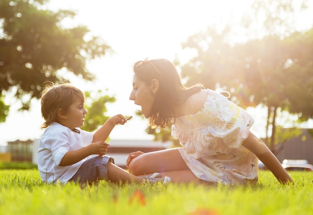 Hermosa joven madre con su hijo comiendo yogur en el parque.