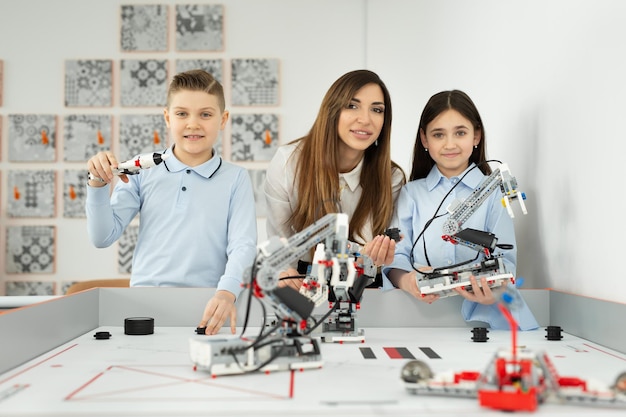 Hermosa joven madre con su hijo e hija posan en la escuela de robótica con robots