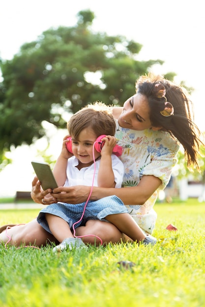 Hermosa joven madre con su hijo escuchando música en el parque.