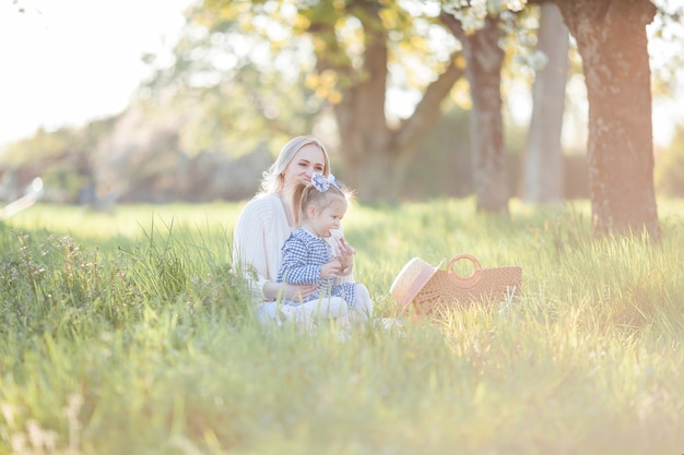 Una hermosa joven madre con su pequeña hija están descansando en un picnic en el jardín de flores