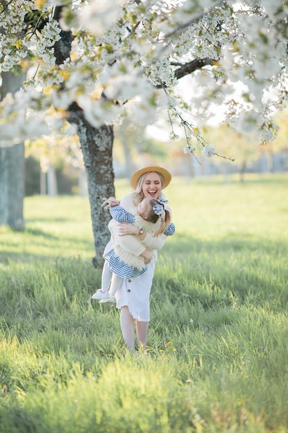 Una hermosa joven madre con su pequeña hija están descansando en un picnic en el jardín de flores