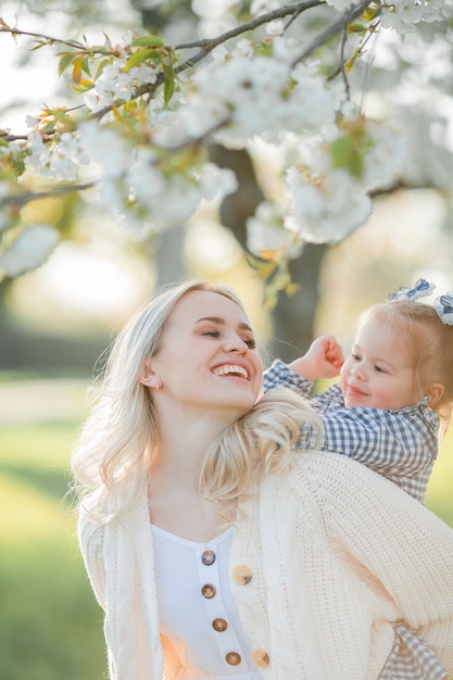 Una hermosa joven madre con su pequeña hija están descansando en un picnic en el jardín de flores