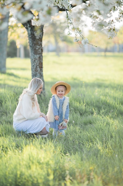 Una hermosa joven madre con su pequeña hija están descansando en un picnic en el jardín de flores