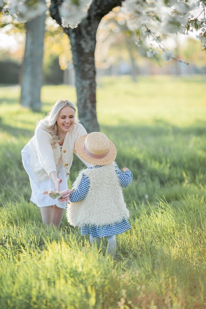 Una hermosa joven madre con su pequeña hija están descansando en un picnic en el jardín de flores