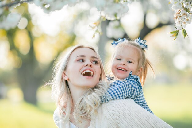 Una hermosa joven madre con su pequeña hija están descansando en un picnic en el jardín de flores