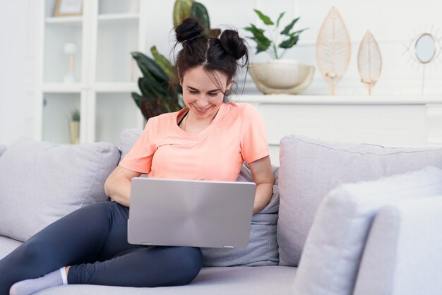 Hermosa joven madre usa una computadora portátil y sonriendo en el sofá en casa