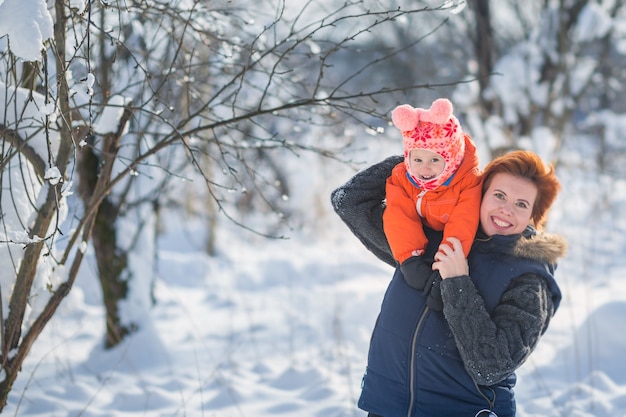 Hermosa joven mamá y su pequeña hija linda se divierten al aire libre en invierno.