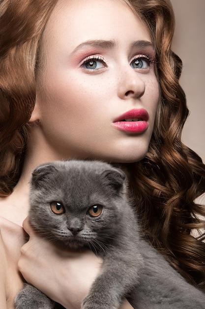 Hermosa joven maquillaje de luz natural y rizos con un gato en sus brazos Cara de belleza