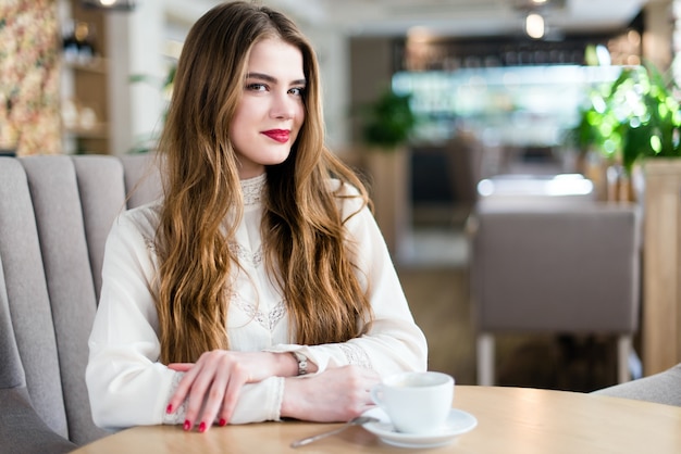 Hermosa joven con maquillaje profesional y peinado sentado en el restaurante.