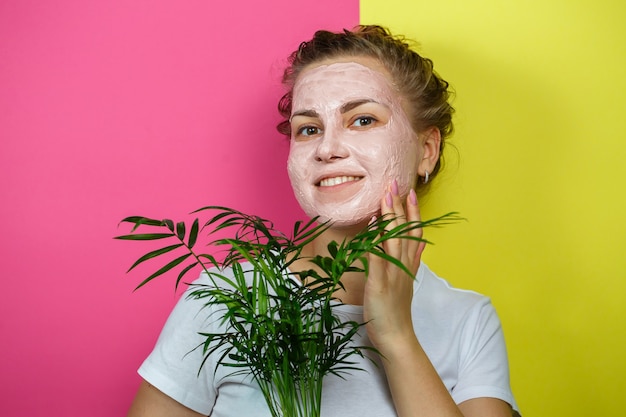 Hermosa joven con una máscara refrescante en su rostro. Sosteniendo una palma decorativa en sus manos. Belleza y piel sana