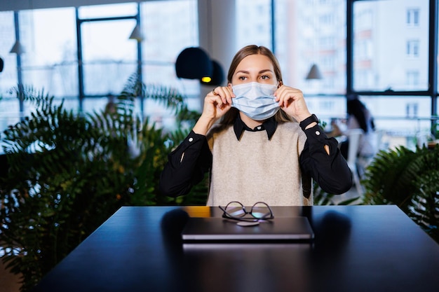 Hermosa joven con una máscara trabajando en un café con una laptop durante la pandemia del coronavirus.