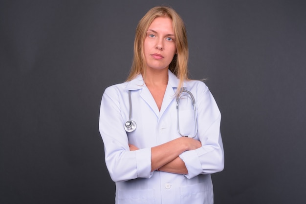 Hermosa joven médico con cabello rubio contra la pared gris