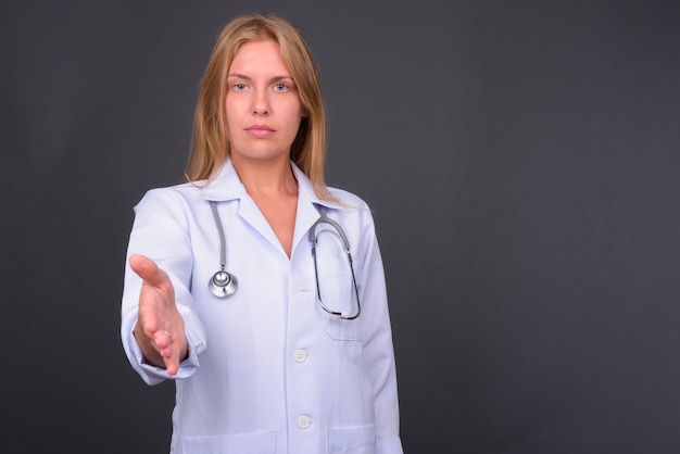 Hermosa joven médico con cabello rubio contra la pared gris